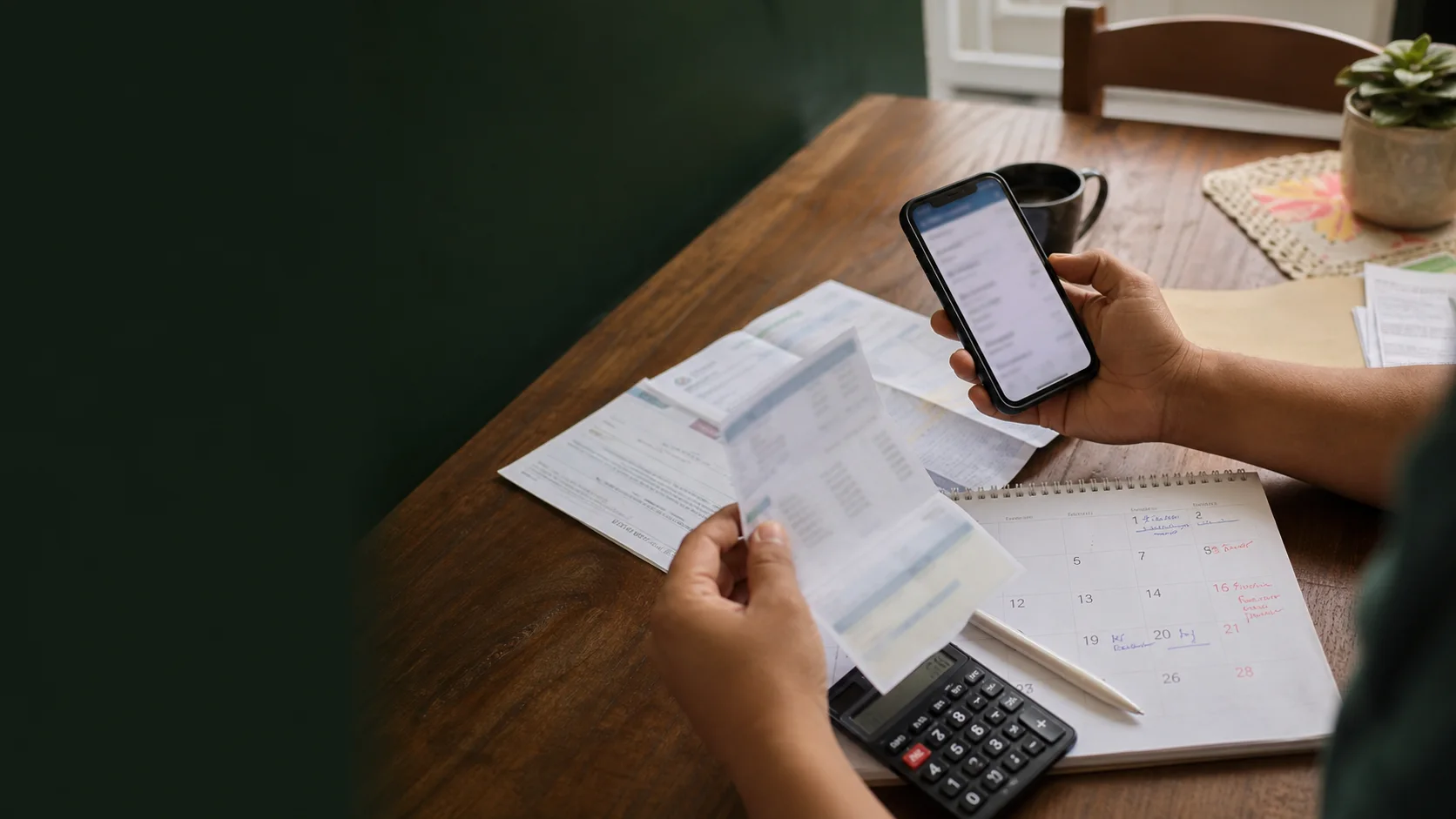 Mãos de uma trabalhadora usando o celular junto a documentos de trabalho sobre uma mesa